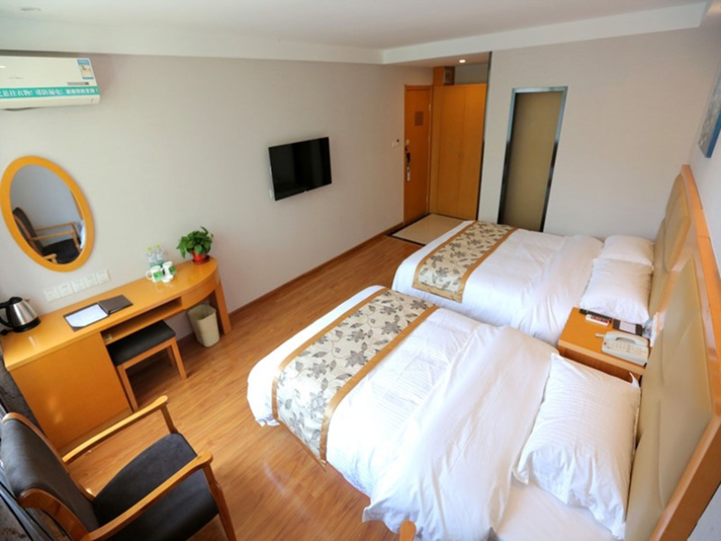 A hotel room with two beds, a desk, a chair, a television, and a mirror.