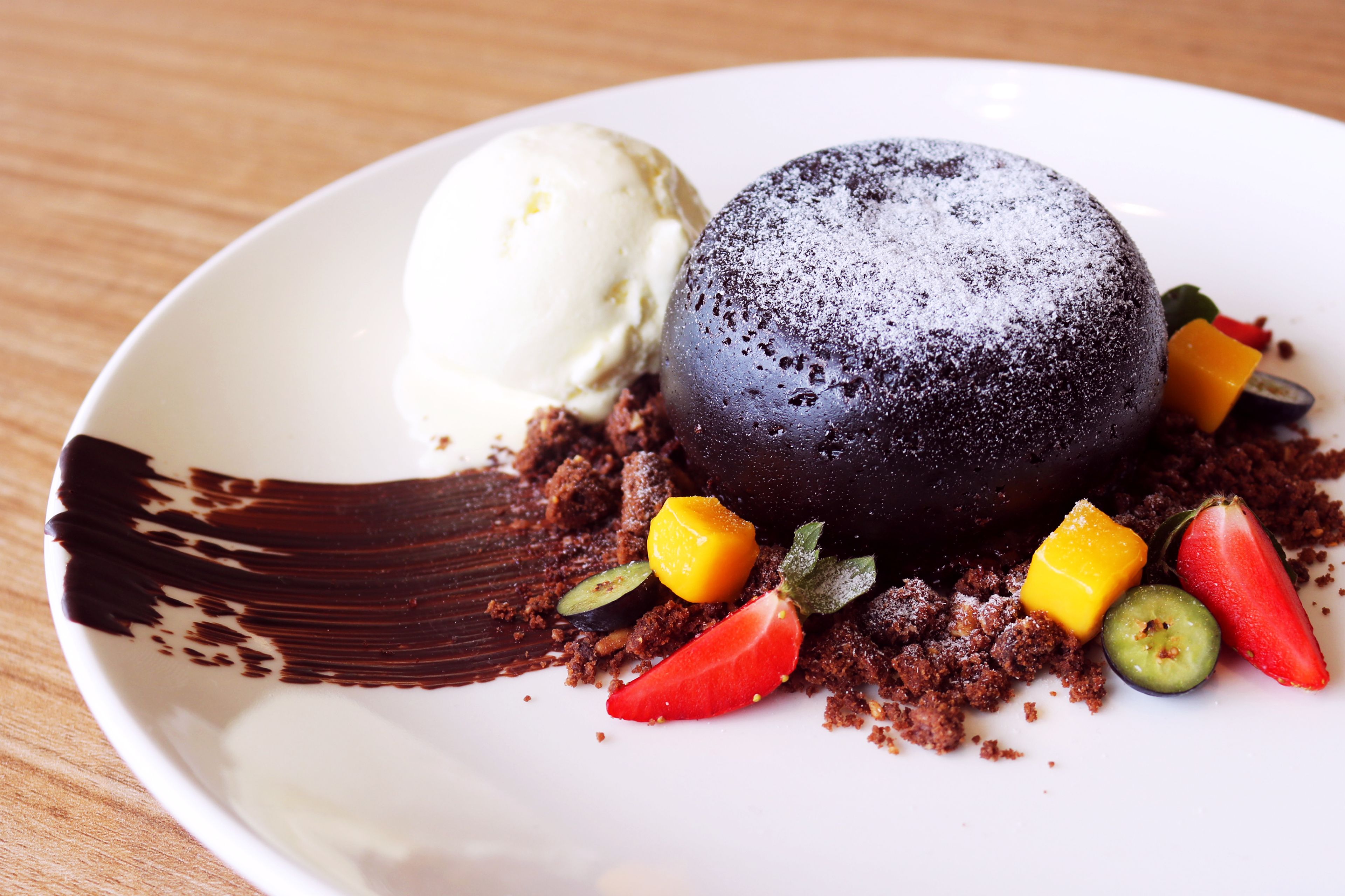 A dessert plate with a chocolate sphere, ice cream, and fruit pieces.