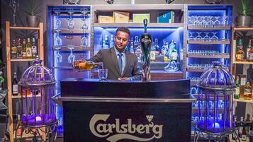 A bar area with a bartender, shelves of liquor bottles, and illuminated glassware.
