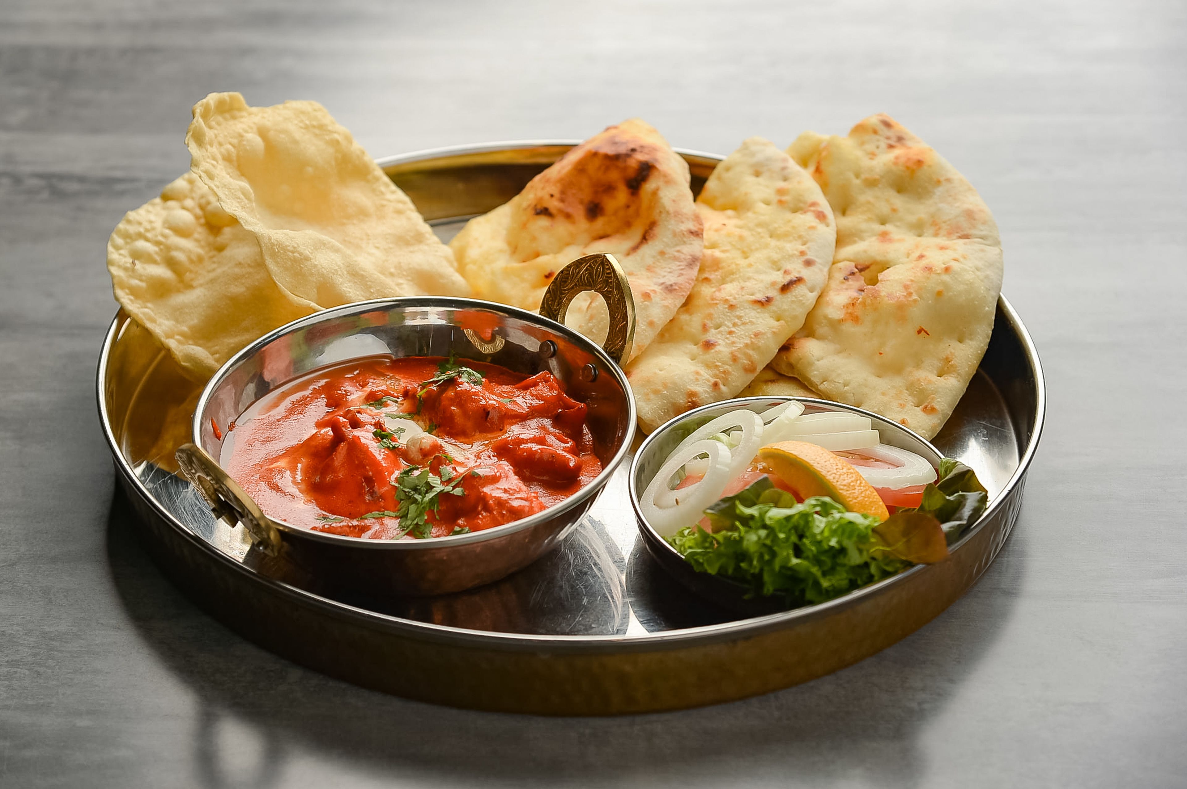 A plate with naan bread, a bowl of red curry, and a side of sliced onions and lettuce.