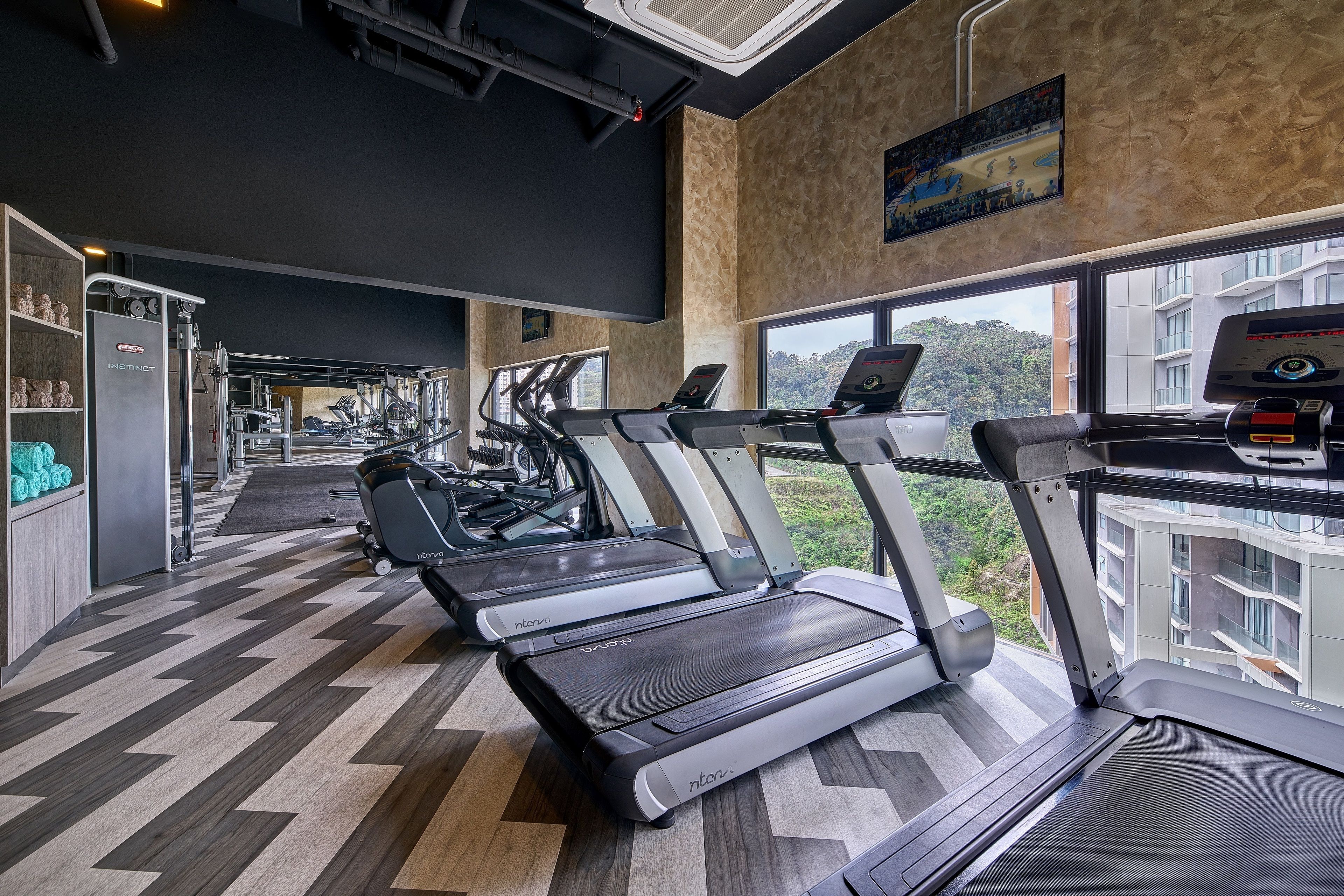 Un gimnasio con cintas de correr, máquinas de pesas y vistas a un edificio a través de amplias ventanas.