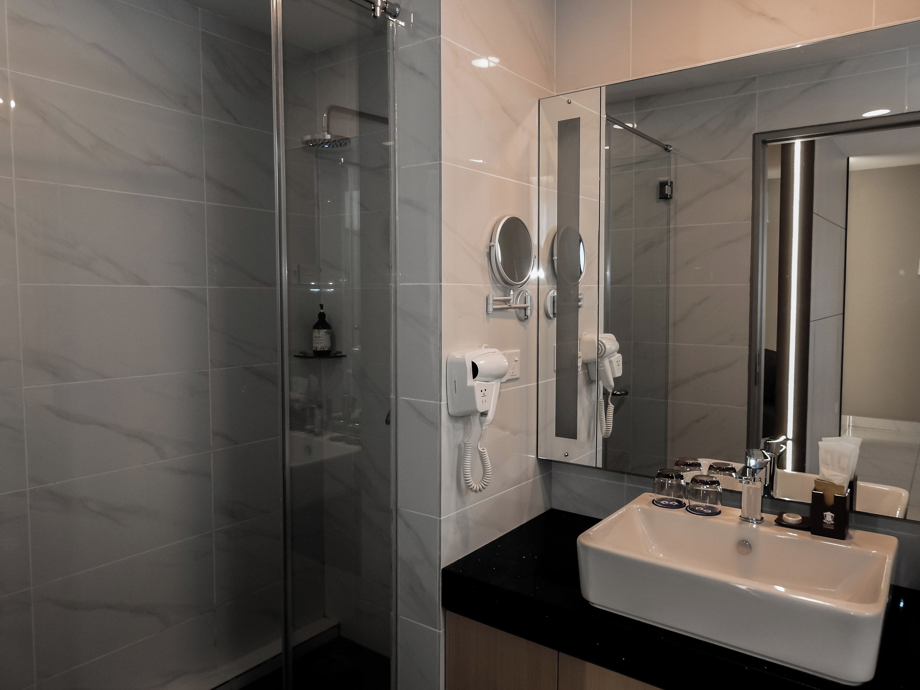 A modern bathroom with a glass-enclosed shower, a white sink, and a large mirror.