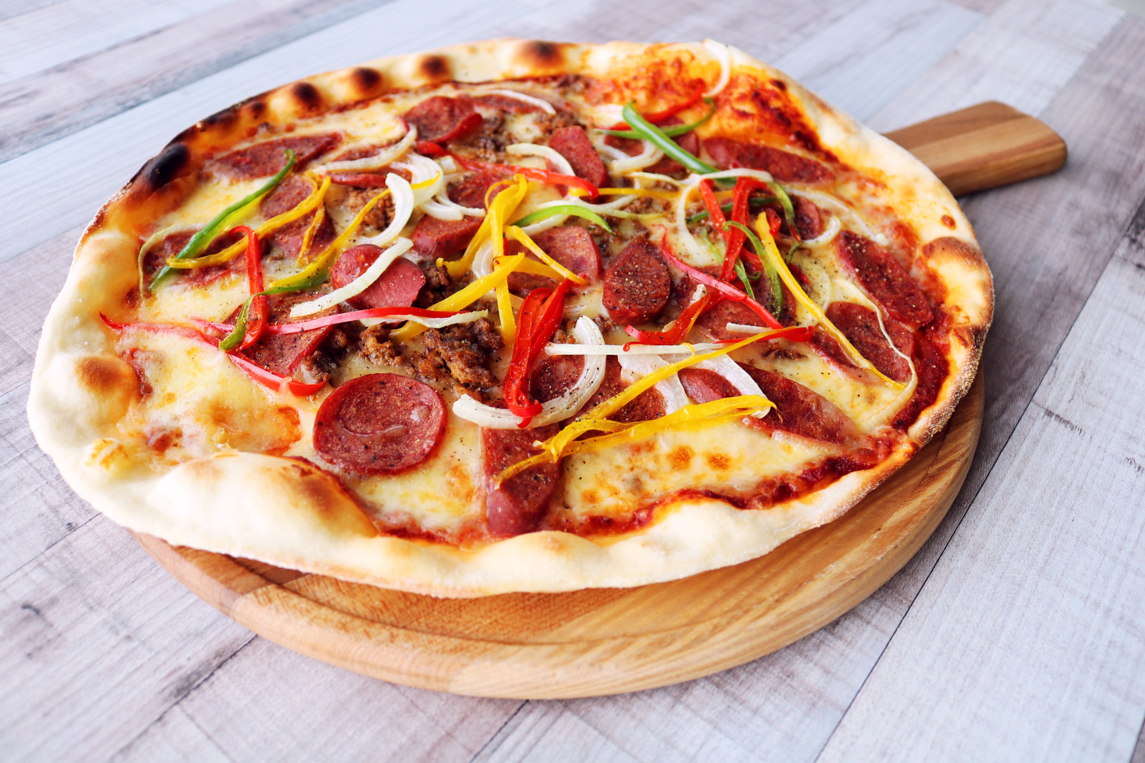 A pizza with pepperoni, bell peppers, and onions on a wooden board.
