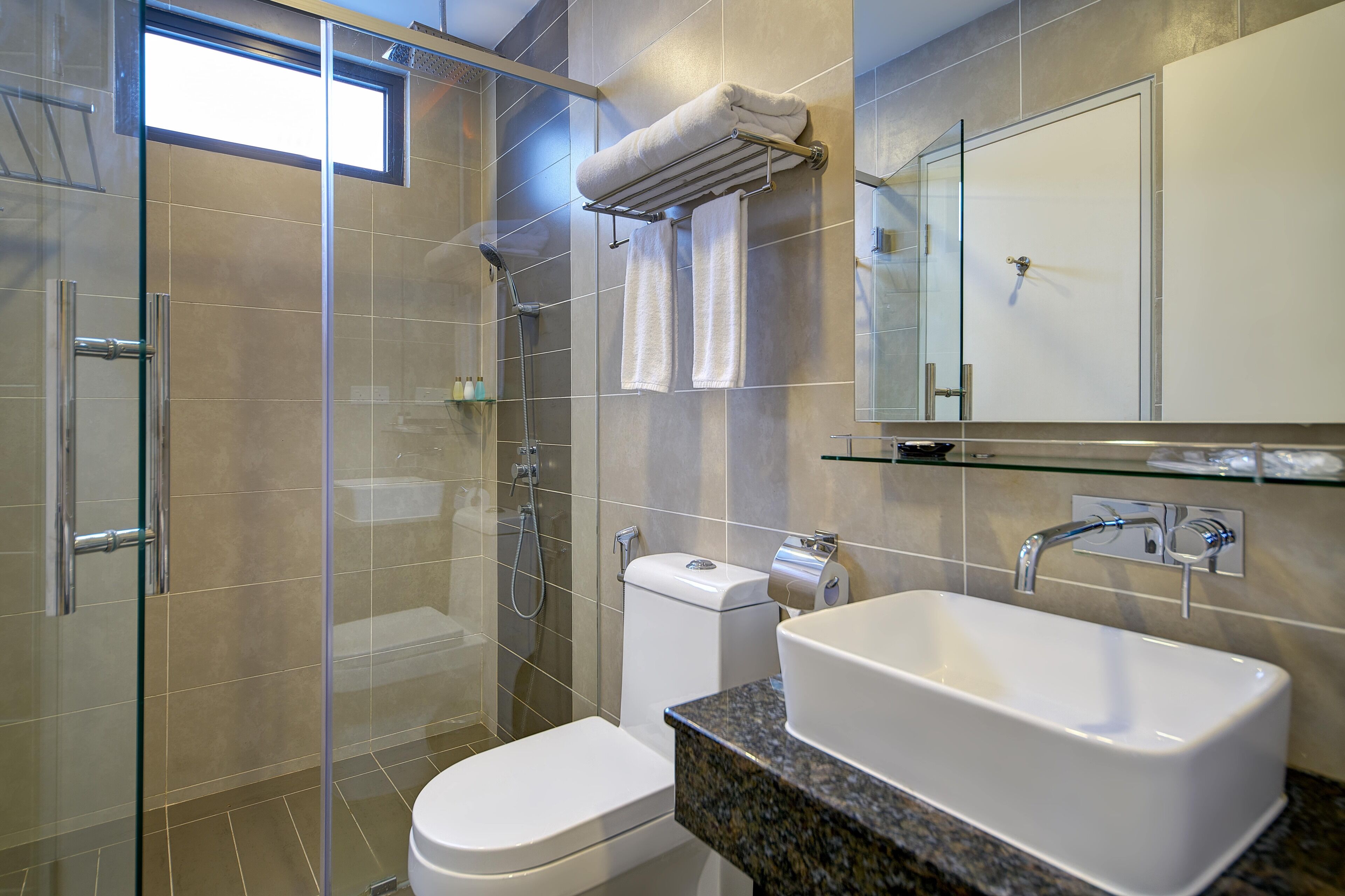 A modern bathroom with a glass shower enclosure, a toilet, a sink with a granite countertop, and a mirror above the sink.