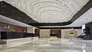 Un hall d’entrée moderne avec un sol en marbre, un comptoir d’accueil et un plafond doté d’un système d’éclairage original.