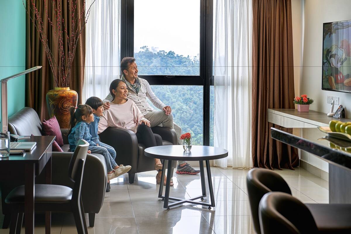 Une famille est assise près d’une grande fenêtre donnant sur un paysage montagneux. On aperçoit dans la pièce un coin repas et un téléviseur.