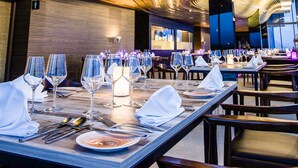 Un restaurant doté d’un plafond au design moderne et aux lignes courbes, et de plusieurs tables où sont disposés des couverts et des verres élégants, créant une ambiance raffinée.