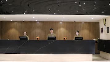 A reception desk with three staff members, wooden panel walls, and a marble countertop.