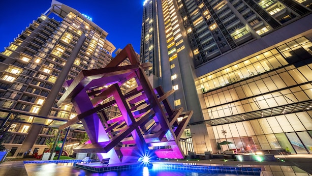 Un hôtel moderne doté d’une sculpture géométrique remarquable dans la cour, entouré d’immeubles de grande hauteur.