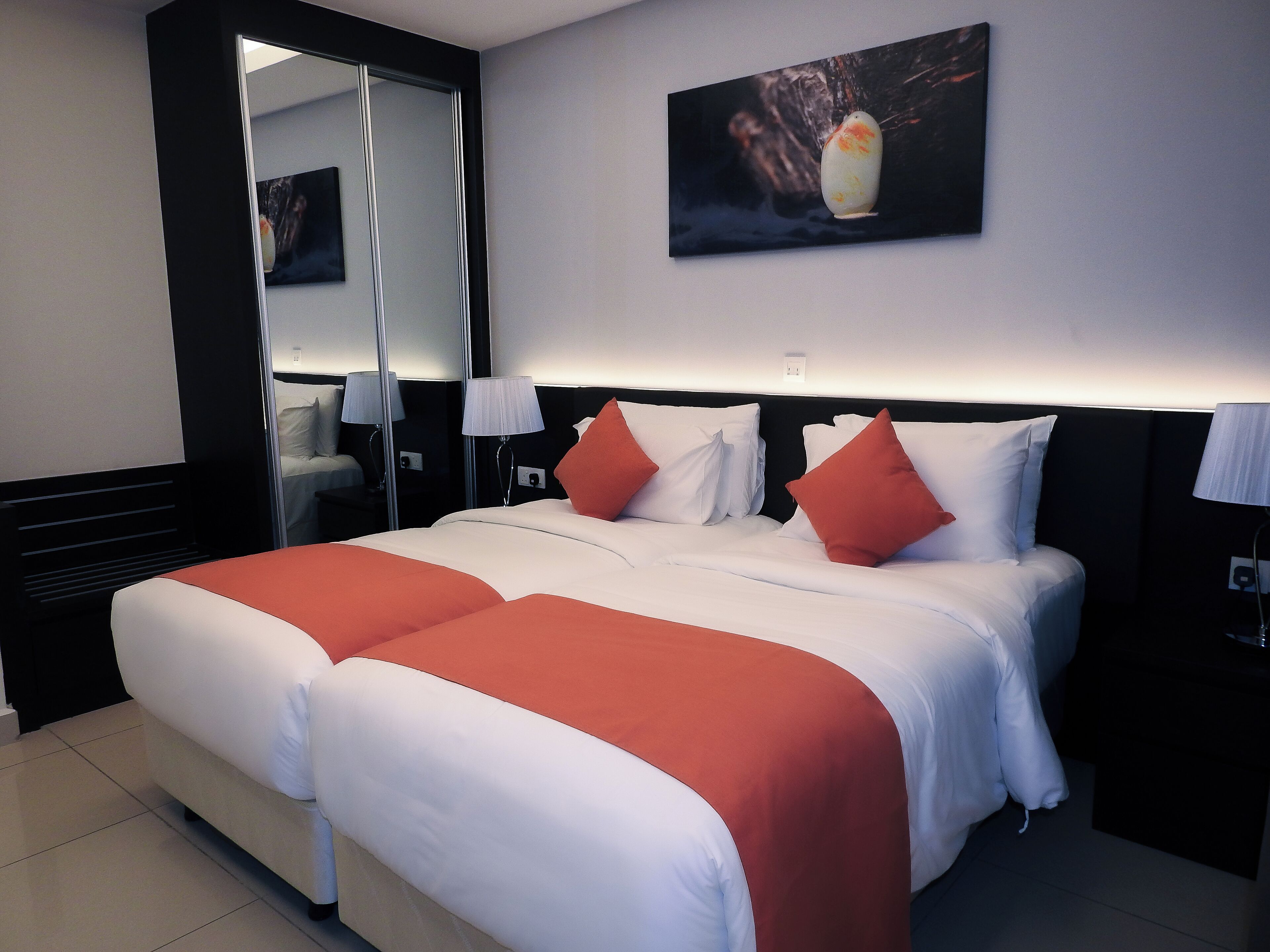 Een hotelkamer met een groot bed, twee nachtkastjes, een spiegel en een schilderij aan de muur.