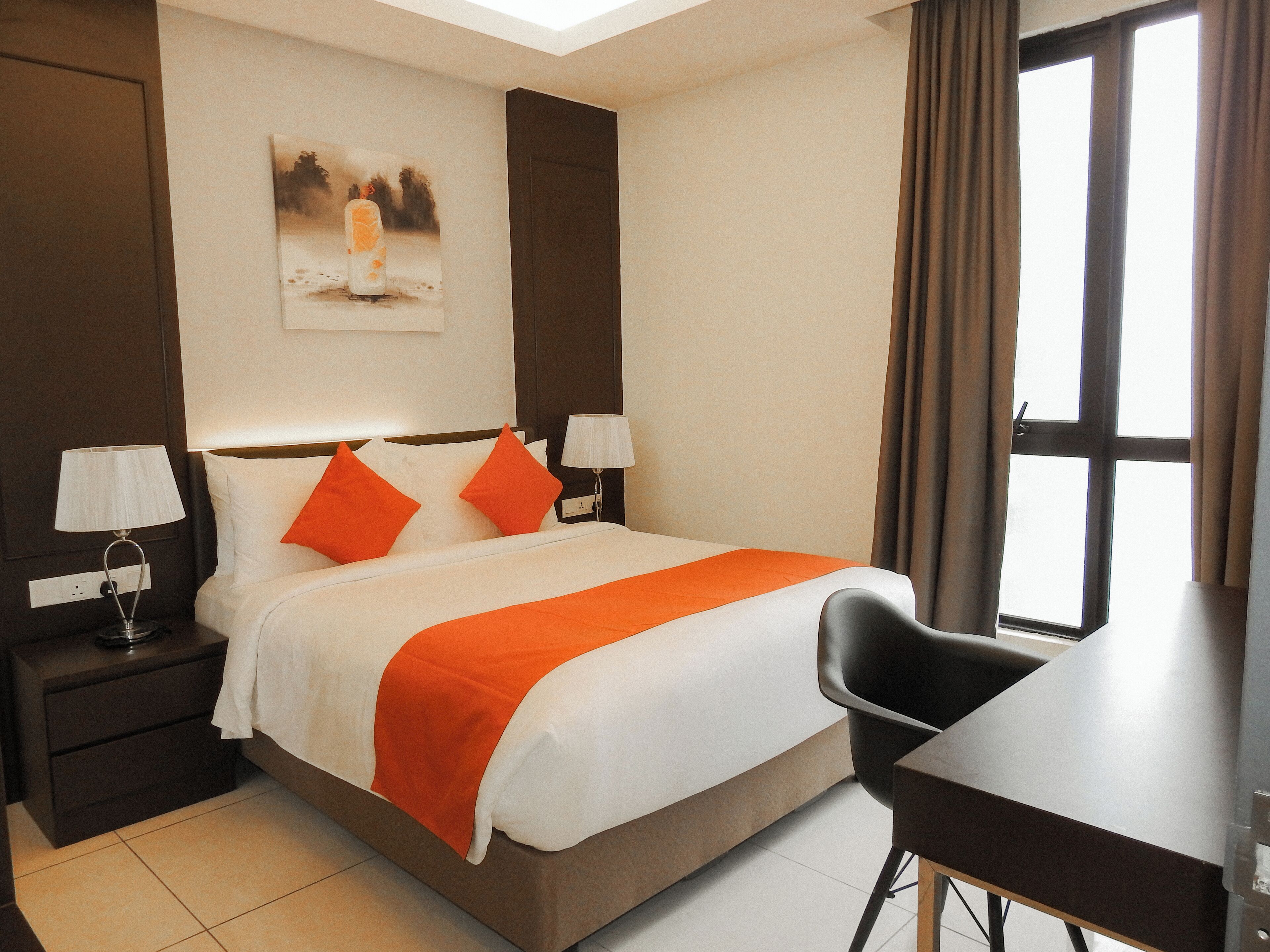 A hotel room with a bed, two bedside tables with lamps, a desk, and a window with curtains.