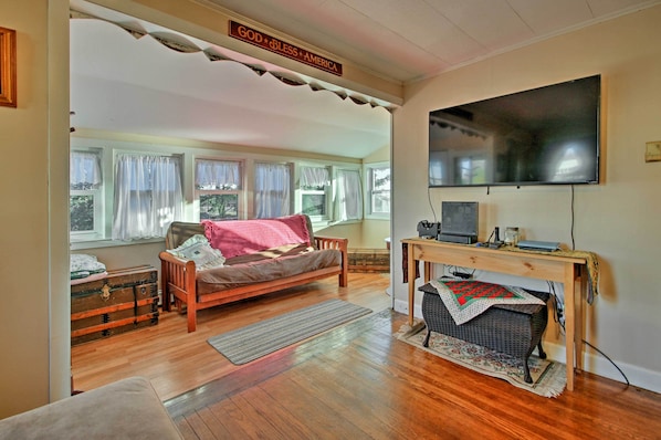 A cozy living room with a wooden sofa, a television, and a desk with a computer. - Steps to Cape Cod Canal: Pet-Friendly Home (Buzzards Bay)