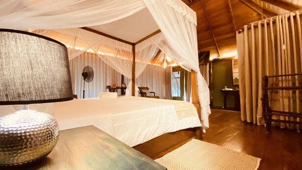 A spacious room with a large bed, a bedside lamp, and a wooden floor. - Yala Lake View Cabanas (Thissamaharama)