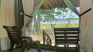 A wooden chair and a bench facing a view of a river and trees. - Yala Lake View Cabanas (Thissamaharama)