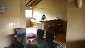 A dining area with a round table and chairs, a kitchen in the background, and a ceiling fan. - Beautiful, new beachfront villa-saltwater pool, gardens, directly on the ocean! (Troncones)