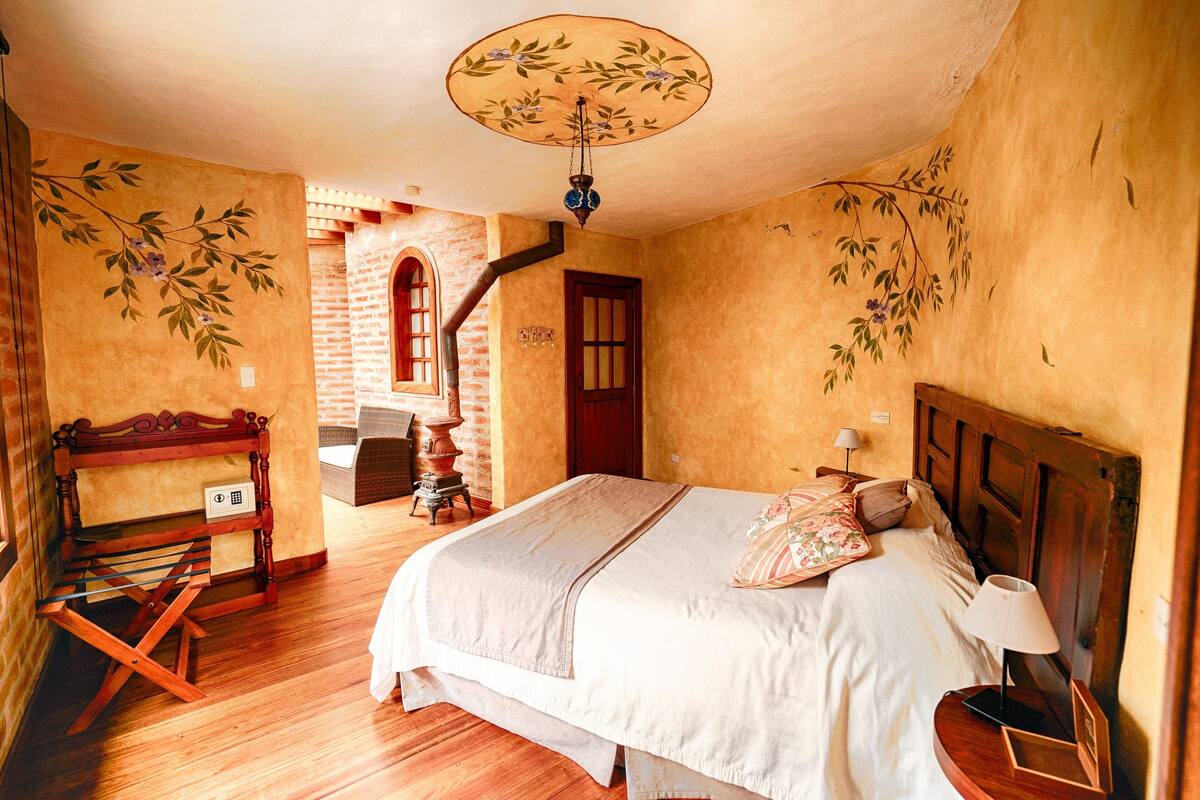 Une chambre à coucher avec un lit en bois, une table de chevet, un banc et une porte donnant sur une autre pièce.