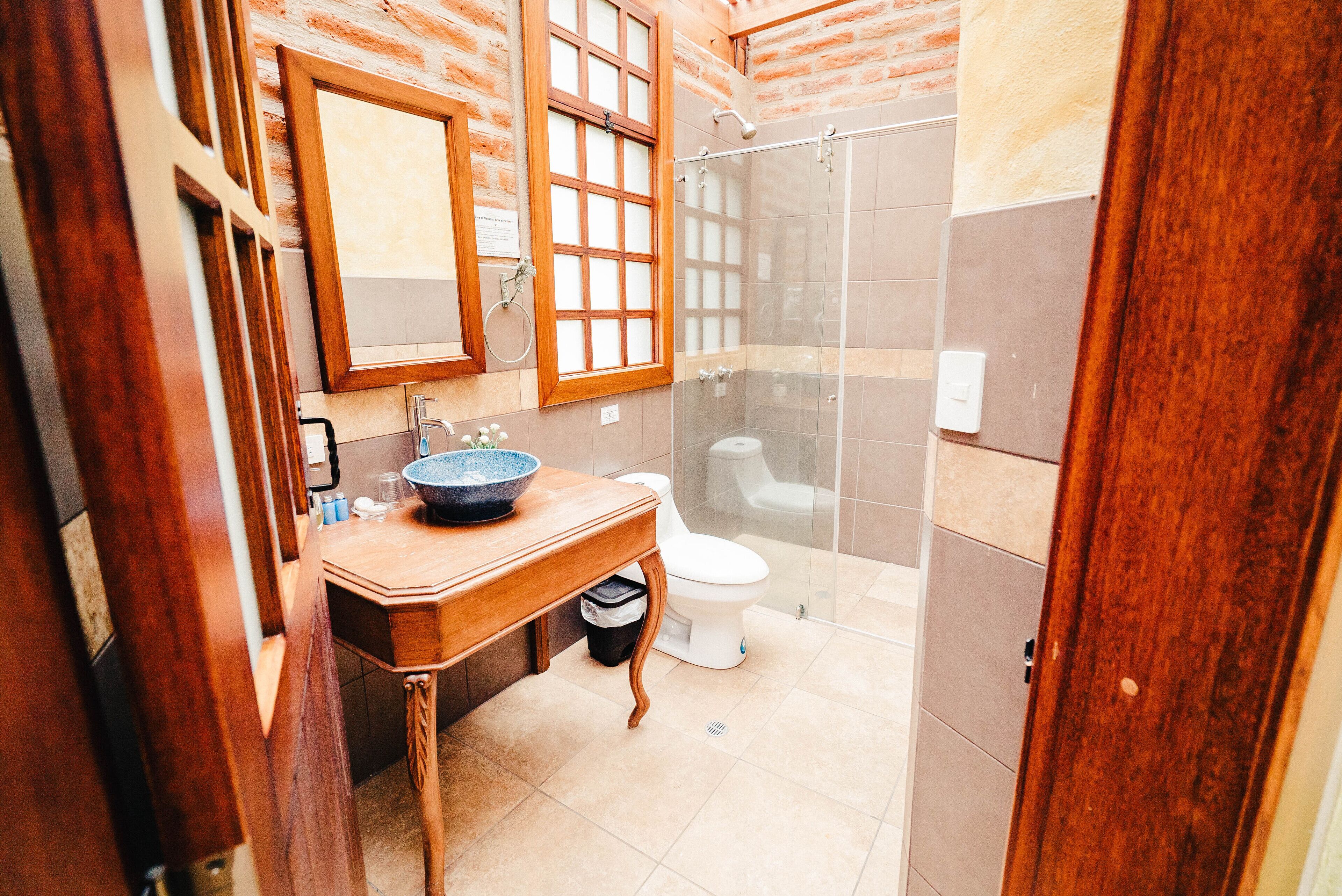Un baño con tocador de madera, un espejo grande, cabina de ducha de vidrio y un inodoro blanco.