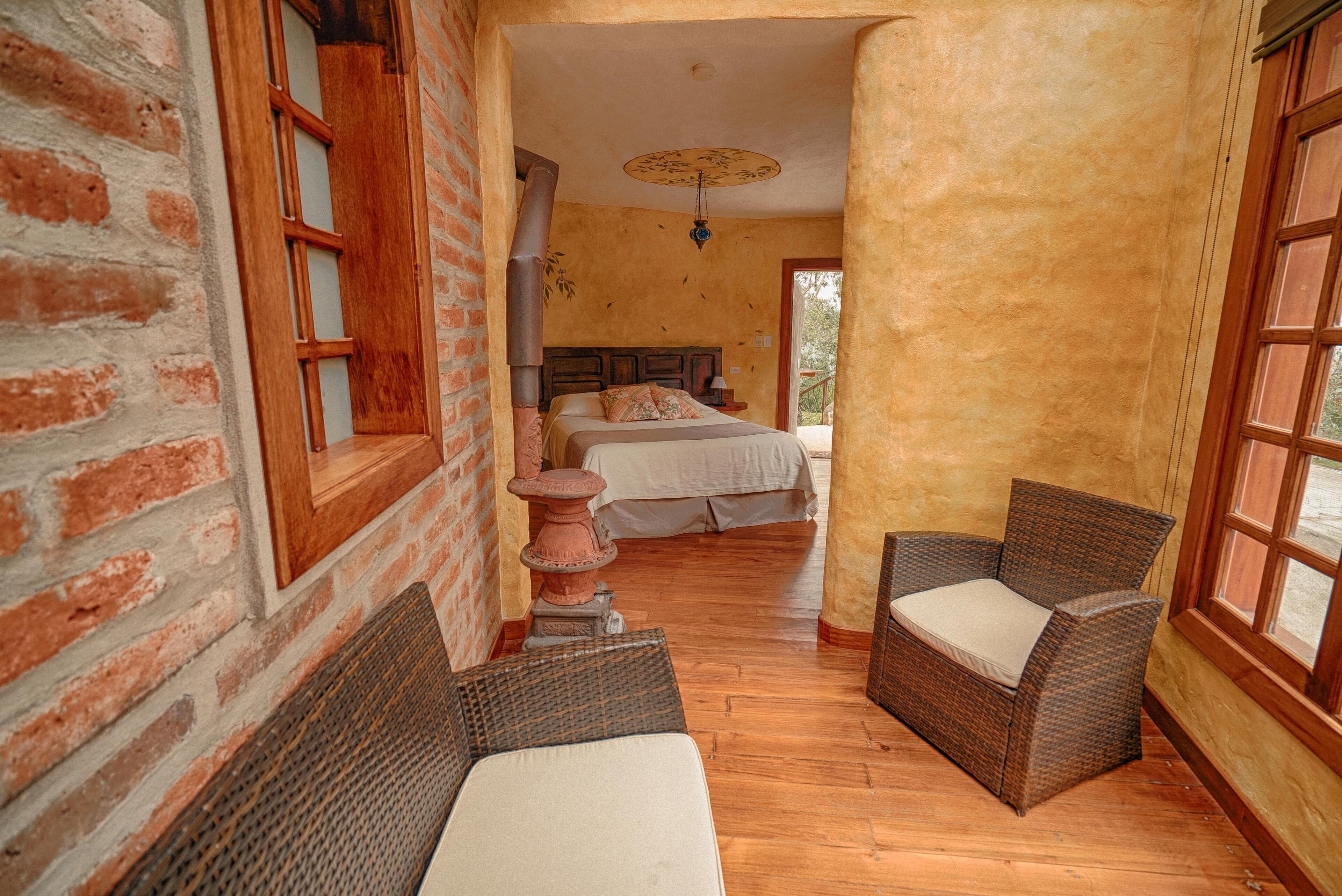 A cozy room with a bed, a wicker chair, and a large window.