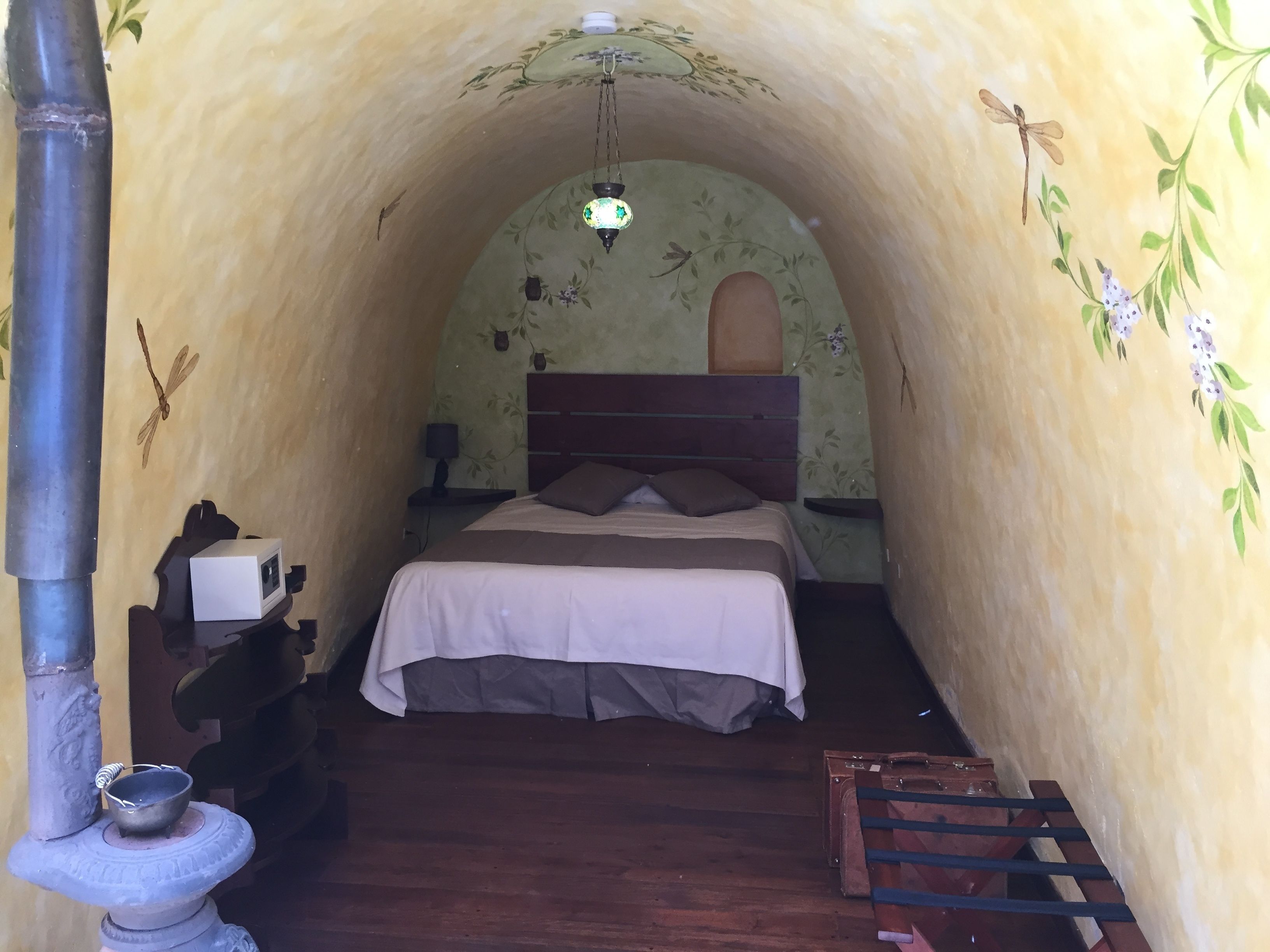 A cozy, arched room with a bed, a small table with a lamp, and a decorative wall.