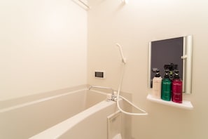 A bathroom with a bathtub, a handheld showerhead, and a shelf with three bottles of shampoo.
