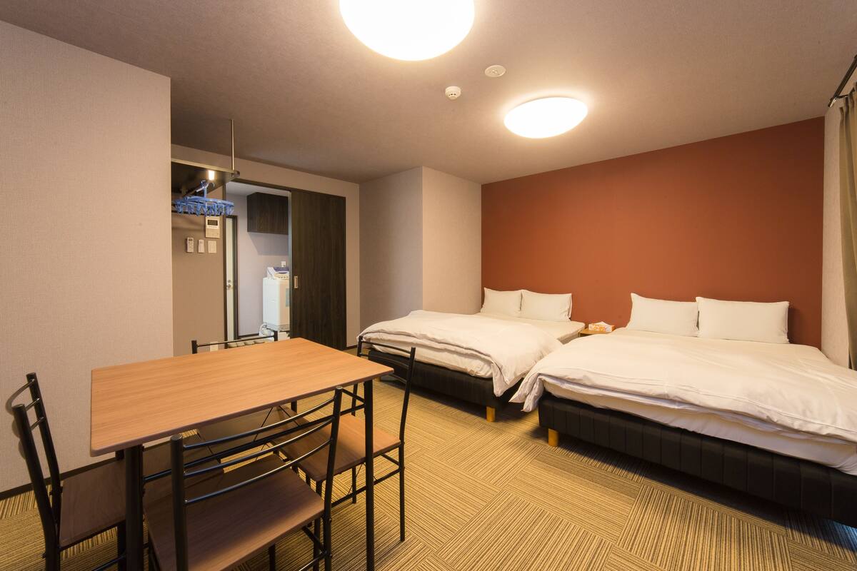 A hotel room with a wooden table and chairs, two beds, and a carpeted floor.