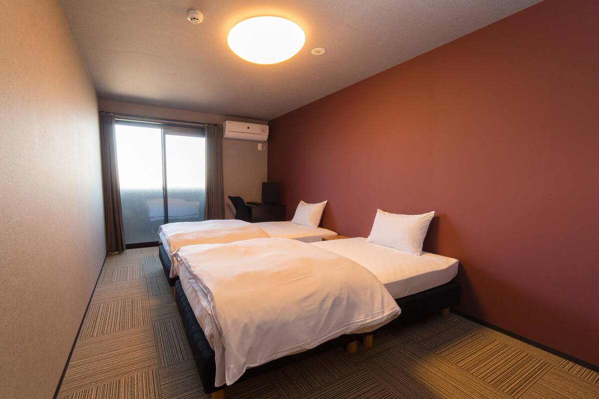 A hotel room with two beds, a desk, and a window.
