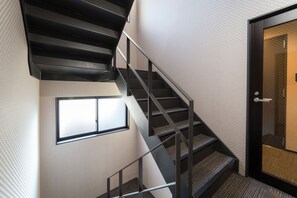 Un escalier moderne avec des rampes en métal et des marches recouvertes de moquette, menant à une porte dotée d’un panneau de verre.