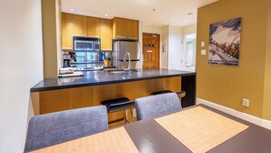 A modern kitchen with wooden cabinets, stainless steel appliances, and a central island with seating. - Aspens #113 Prime Ski-in Ski-out Location! Pool, Hot tubs, BBQ, sleeps 4 (Whistler)