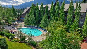 A resort with a swimming pool surrounded by tall trees and a mountain backdrop. - Aspens #113 Prime Ski-in Ski-out Location! Pool, Hot tubs, BBQ, sleeps 4 (Whistler)
