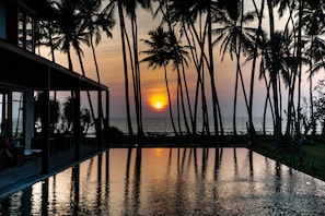 A sunset view from a poolside area with palm trees and a building in the background. - The Villa by Contemporary Ceylon (Wadduwa)