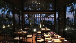 A dining area with tables set for service, large windows offering a view of palm trees and the ocean, and a ceiling fan. - The Villa by Contemporary Ceylon (Wadduwa)