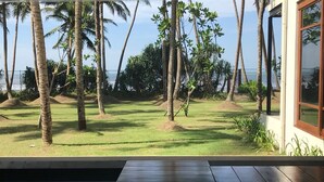A poolside view with a wooden deck, palm trees, and a building with large windows. - The Villa by Contemporary Ceylon (Wadduwa)