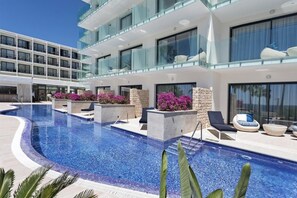 A modern hotel with a large outdoor swimming pool, multiple balconies with glass railings, and outdoor seating areas with lounge chairs and planters. - Catalonia Royal Ses Estaques (Santa Eulalia del Rio)