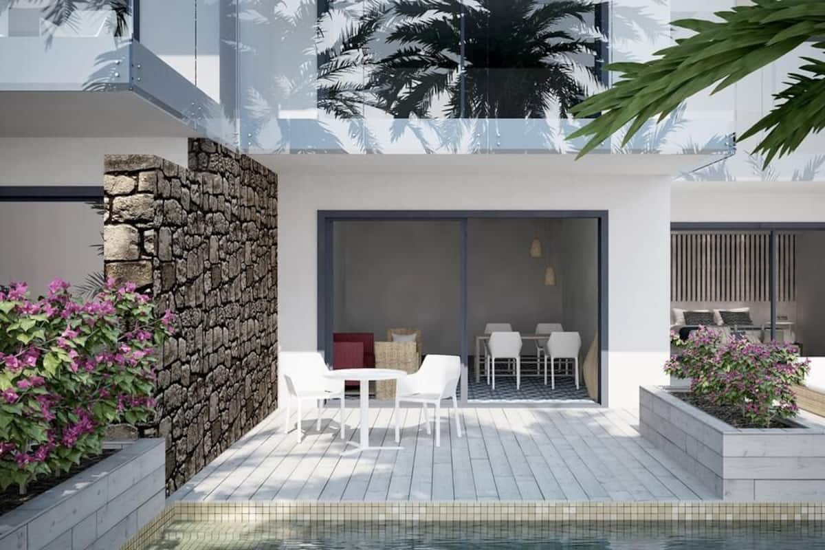 A modern outdoor pool area with stone walls, white furniture, and tropical plants.