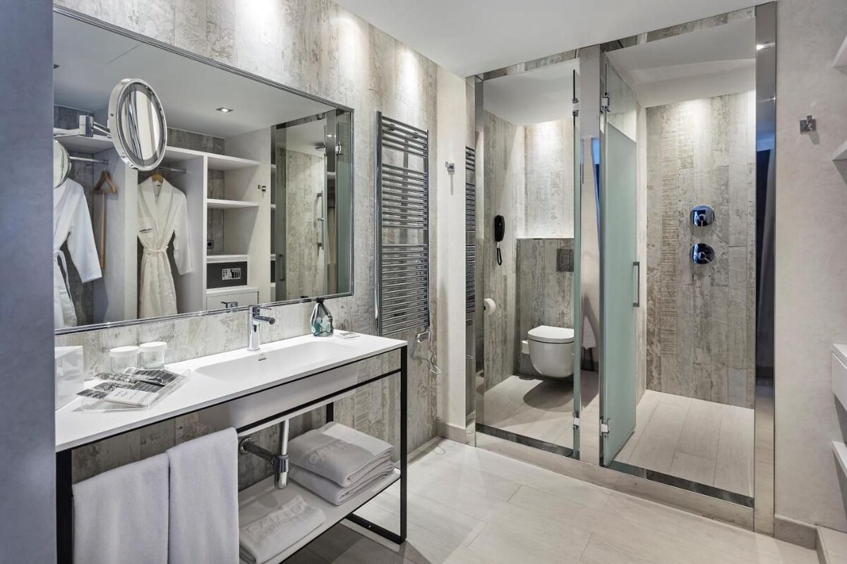 A modern bathroom with a glass-enclosed shower, a large mirror, and a vanity with a sink and towel rack.
