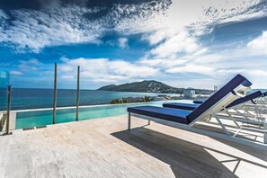 A poolside area with lounge chairs and a view of the sea and a distant island. - Catalonia Royal Ses Estaques (Santa Eulalia del Rio)