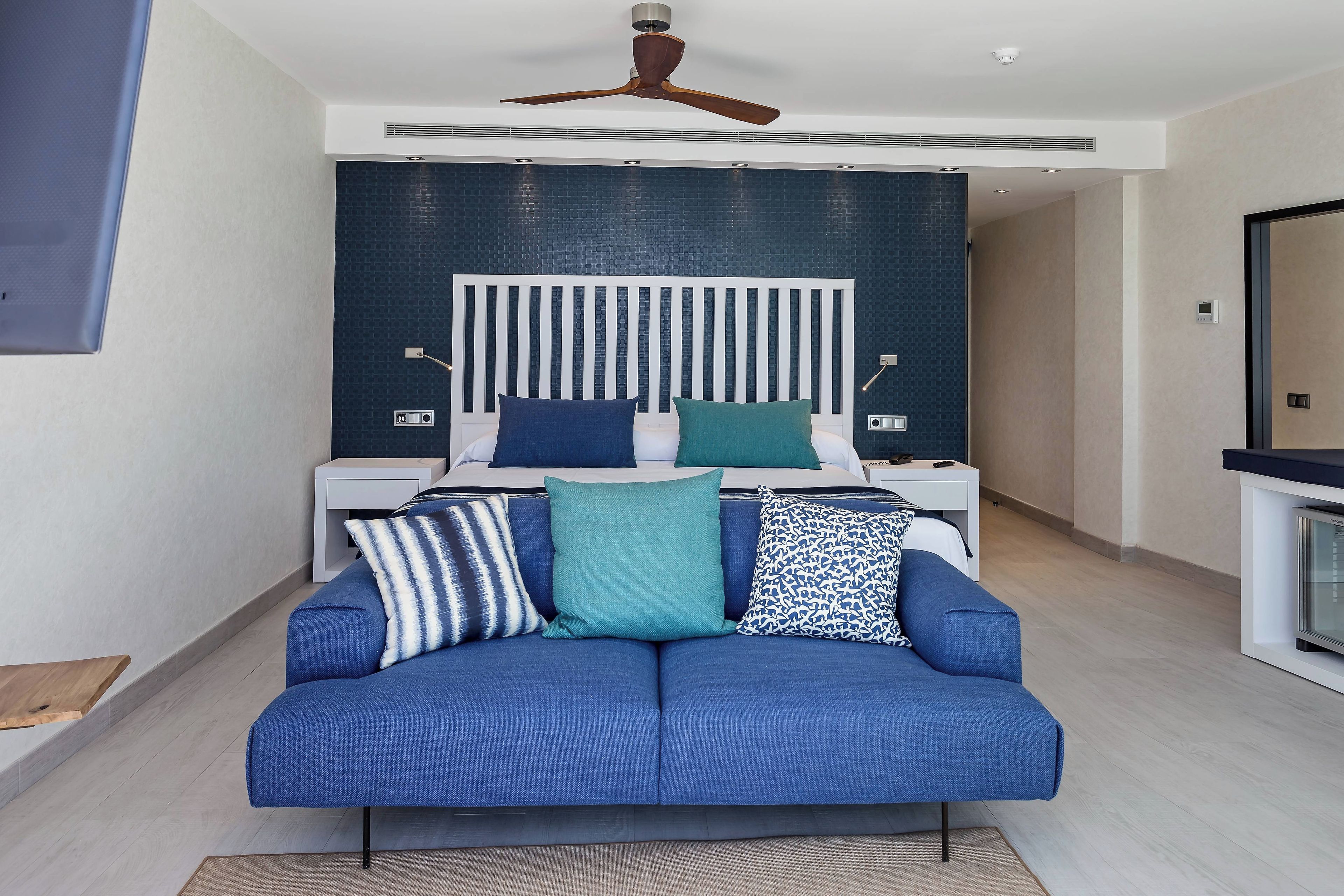 Ein modernes Schlafzimmer mit einem Bett, einem blauen Sofa, einem Deckenventilator und einem Nachttisch mit einer Lampe.
