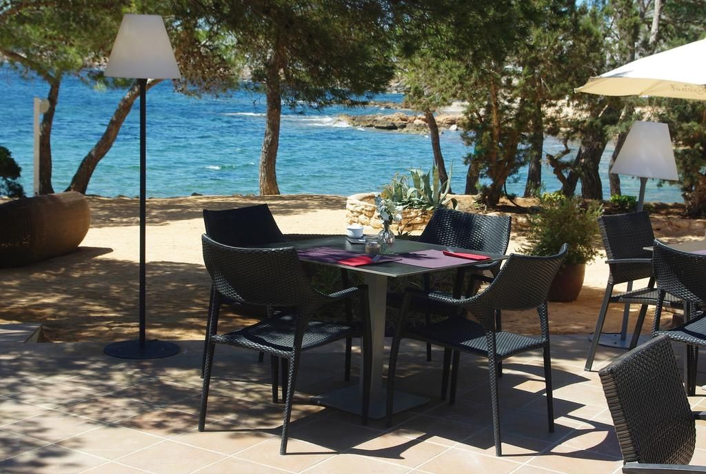 Un espace de restauration en plein air, avec une table et des chaises, entouré d’arbres et offrant une vue sur un plan d’eau.