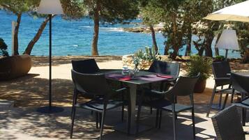 Un espace de restauration en plein air, avec une table et des chaises, entouré d’arbres et offrant une vue sur un plan d’eau.