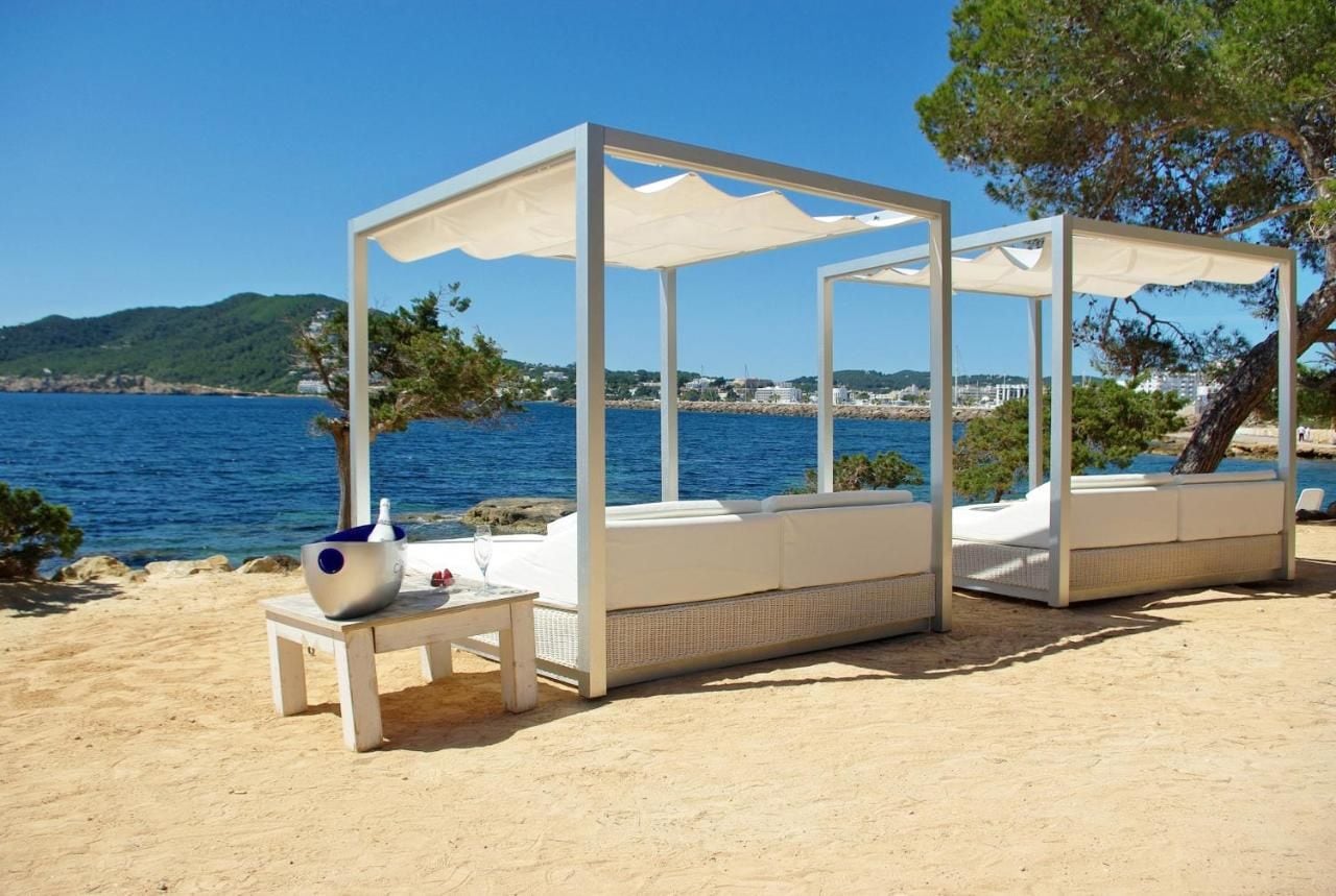 Un espace aménagé avec des sièges, situé en bord de plage, doté de parasols blancs et de meubles en osier, offrant une vue sur le paysage côtier.