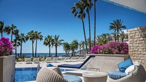 Un espace aménagé au bord de la piscine, avec des chaises longues, une petite piscine et des palmiers.
