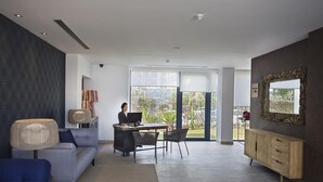 Un salon moderne avec un canapé, un bureau équipé d’un ordinateur et une grande fenêtre donnant sur l’extérieur.