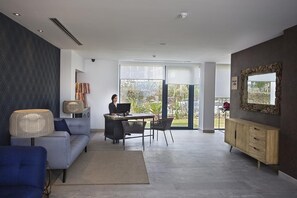 A modern living room with a sofa, a desk with a computer, and a large window offering a view of the outdoors. - Catalonia Royal Ses Estaques (Santa Eulalia del Rio)