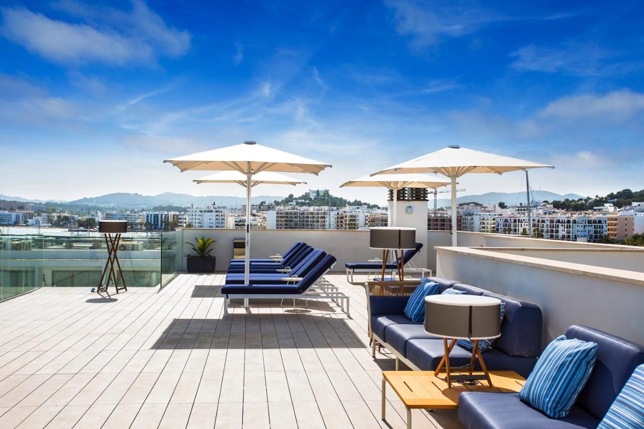 A rooftop terrace with sun loungers, umbrellas, and a sofa.