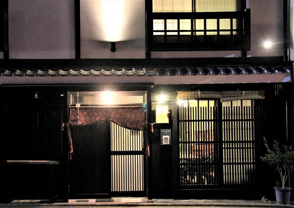 A traditional Japanese building with a dark wooden gate, a tiled roof, and a small potted plant.