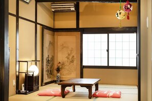 Une pièce traditionnelle japonaise avec un sol recouvert de tatamis, une table basse, un paravent shoji et une décoration florale suspendue.