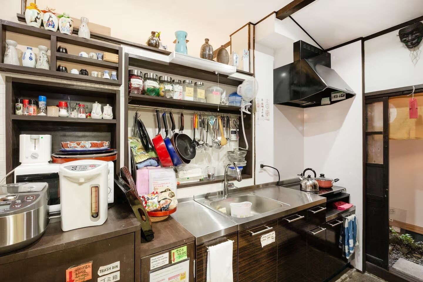 A kitchen with a stainless steel sink, a stove, and various kitchen utensils and appliances.