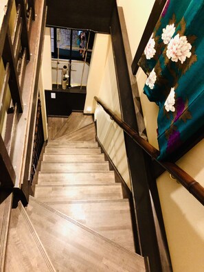 A wooden staircase with a handrail, leading to a room with a window and a map on the wall.