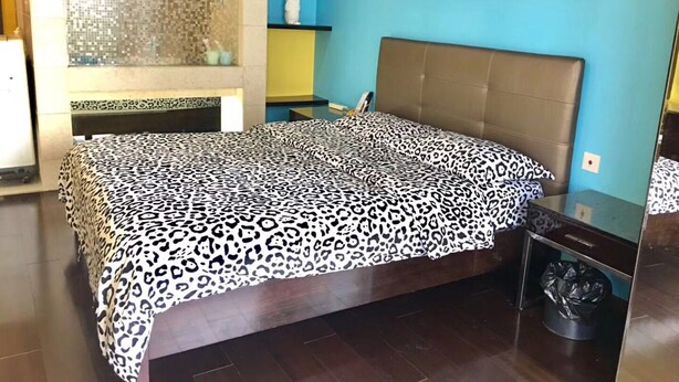 A bedroom with a bed, a bathroom with a shower, and a wall-mounted shelf with toiletries.