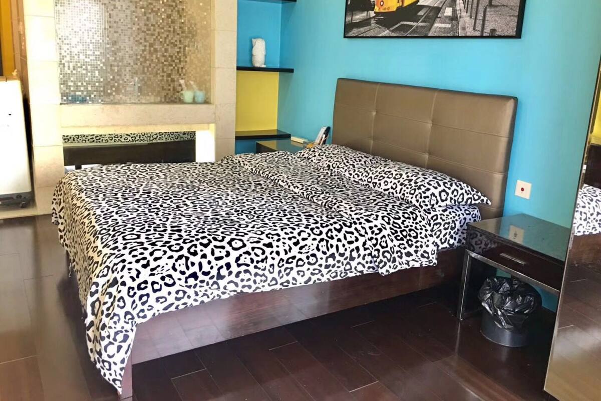 A bedroom with a bed, a bathroom with a shower, and a wall-mounted shelf with toiletries.